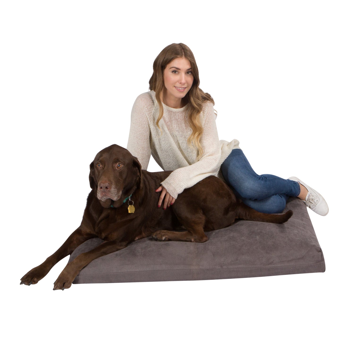 A woman in a white sweater and jeans sits on the Orthopedic Memory Foam Dog Bed next to a chocolate Labrador Retriever, gently petting her dog. Both look toward the camera against a white background.