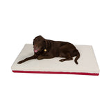 A brown dog lies on the 100% Natural Materials Orthopedic Dog Bed—a rectangular, white and red bed—looking at the camera with its tongue out.